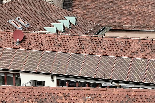 Rote Photovoltaikanlagen fallen neben den roten Dachziegeln einer Altstadt kaum auf.