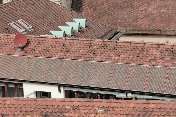 Rote Photovoltaikanlagen fallen neben den roten Dachziegeln einer Altstadt kaum auf.